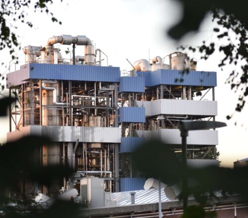 Industrieel complex met metalen pijpleidingen en tanks onder een blauwe lucht.